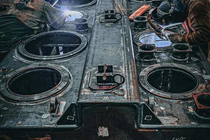 Zwei Arbeiter sind in einer Fabrik damit beschäftigt, große Metallkomponenten zu schweißen.