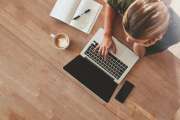 Top view of woman using laptop while sitting at cafe table with laptop, mobile phone, diary, coffee cup and glasses. Female surfing internet at coffee shop.