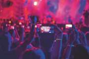 a group of youth dancing with their hands up and taking videos and photos on the phone at a street music festival,blurred background
