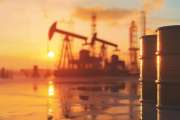 Oil barrels and drilling rigs at sunset. Industrial site with equipment against sunset sky reflection. Energy industry concept.