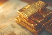 Stack of gold bars next to financial newspaper with stock market updates and gold trading headlines