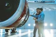 In a Hangar Aircraft Maintenance Engineer Shows Technical Data on Tablet Computer to Airplane Technician, They Diagnose Jet Engine Through Open Hatch. They Stand Near Clean Brand New Plane.