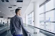 Well dressed young man travel by airplane. Businessman with luggage walking on travelator at airport.