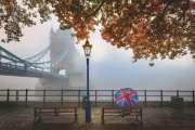 London in autumn concept with a tourist holding a british flag umbrella in front of the famous Tower Bridge during a foggy day