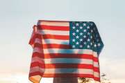 Independence day. Silhouette of woman holds an American flag in her hands, raised above her head. Back view. In the background, sunset sky. Concept of American National Holidays.