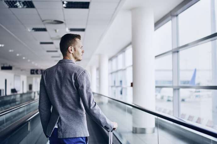 Well dressed young man travel by airplane. Businessman with luggage walking on travelator at airport.