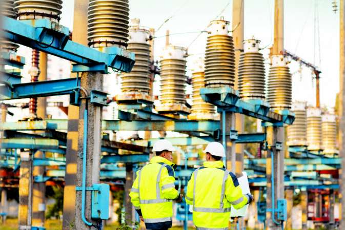 Engineers men in warm clothes use digital tablet computer discuss work walking against power electric substation.