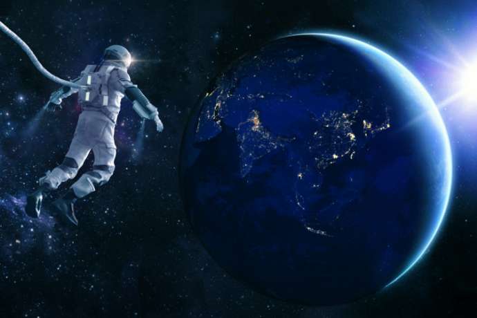 An CG astronaut in a modern space suit, connected to a tethered lifeline floats in deep space and looks at the lights of planet earth as the sun rises. Distant stars and galaxies are visible in the background. Credit: NASA https://earthobservatory.nasa.gov/images/79790/city-lights-of-asia-and-australiaand ESO for background images.