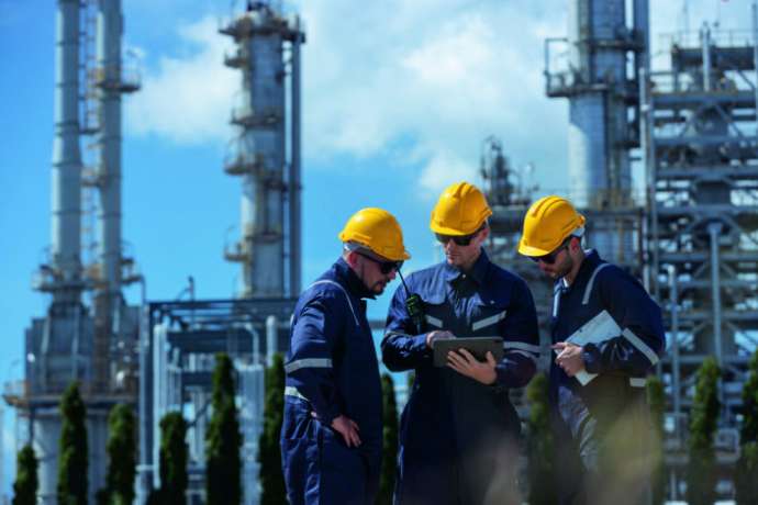 Engineer working using tablet together at station refining oil petrochemical. Technician worker check quality oil industry factory. Inspector standing at zone gas with refinery building background.