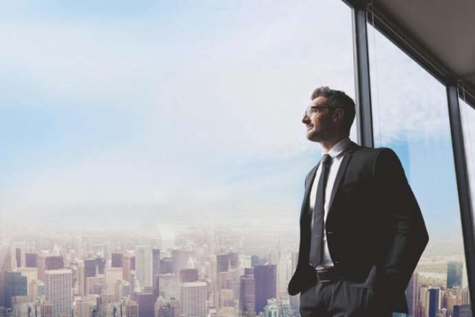 Shot of a handsome mature man looking out from a large window in the office