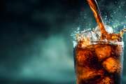 A dynamic image of cola cascading into a tall glass filled with ice, showcasing refreshing splashes and bubbly textures against a dark background.