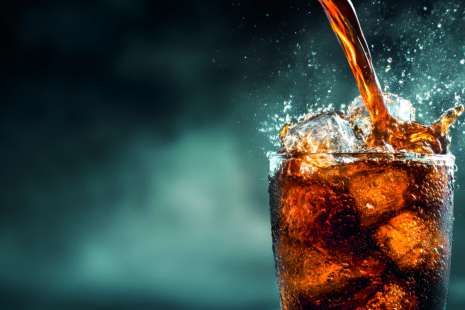 A dynamic image of cola cascading into a tall glass filled with ice, showcasing refreshing splashes and bubbly textures against a dark background.