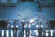 Brand New Airplane Standing in a Aircraft Maintenance Hangar while Aircraft Maintenance Engineer/ Technician/ Mechanic goes inside Cabin via Ladder/ Ramp.