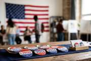 Voting pins on table at US polling station with poll workers, voters and privacy booths in the blurred background during election day